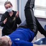 Fysioterapeutti opastaa ja urheilija tekee kehonhallinnan harjoituksia selällään maassa