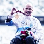 Pyörätuolikelaaja Toni Piispanen esittelee kultamitaliaan Tokion paralympialaisten mitalienjaon jälkeen hymy kasvoilla.