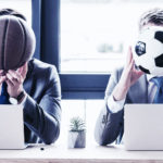 Kaksi miestä istuu toimistossa tietokoneidensa takana ja pitää palloa naamansa edessä - koripalloa ja toinen jalkapalloa.