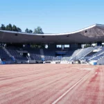 Tyhjä Hippoksen pesäpallostadion. Punaruskea pelikenttä, jonka takana on katsomo. Sininen taivas.